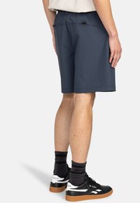 Mörkblå shorts gjorda av lätt material med resårmidja, med fram- och bakfickor, samt sömnadsdetaljer. Svarta sneakers med vita accenter.