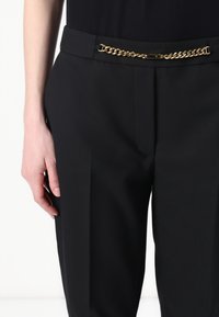Zwarte taillepantalons met een strak design, textuurstof en een gouden kettingriemaccent bij de tailleband.