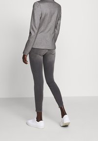 Szary, dopasowany żakiet z teksturowanej tkaniny, sparowany z szarymi dżinsami slim-fit i białymi sneakersami, zaprezentowany od tyłu.