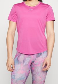 Camisa rosa de manga corta hecha de tela suave, con cuello redondo y logo blanco de Nike en el pecho, combinada con leggins de patrón multicolor.