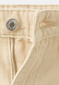 Pantaloni beige in denim con una cerniera metallica visibile e chiusura a scatto. Il tessuto ha una trama strutturata, con dettagli di cuciture sulle giunture.