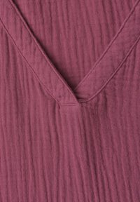 Close-up of textured mauve fabric with a V-shaped neckline and visible seam details.