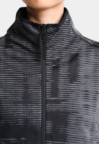 Veste zippée noire en tissu texturé avec des rayures horizontales grises. Col montant et détail de fermeture éclair à l'avant sont visibles.