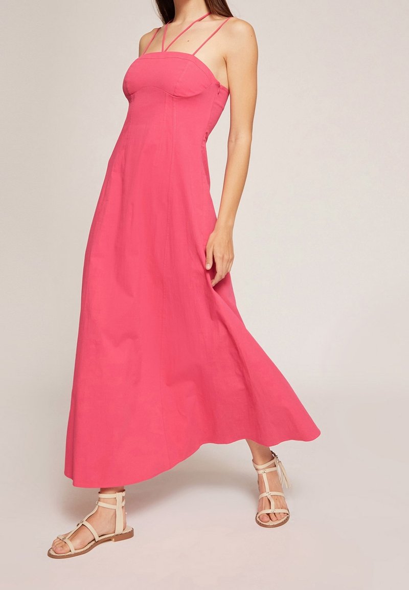 Maxi šaty v jasně růžové barvě, s tenkými ramínky, přiléhavým korzetem a splývavou sukní. V kombinaci s béžovými sandály na špagetových páscích.
