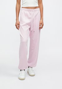 Ροζ ανοιχτόχρωμο παντελόνι φόρμας από απαλό ύφασμα, με ελαστική μέση και κορδόνια, εφαρμογή σε χαλαρή γραμμή, συνδυασμένο με λευκά αθλητικά παπούτσια.