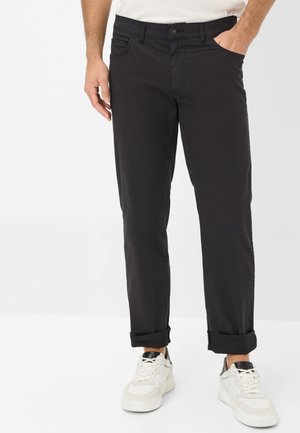 Black cotton trousers with a straight cut, front pockets, and rolled cuffs. Worn with white sneakers featuring black accents.