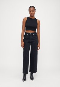 Top cropped preto e jeans pretos de cintura alta com um acabamento texturizado, apresentando acentos brilhantes e design de pernas largas. Botas pretas de bico fino.
