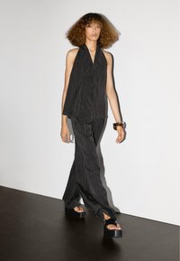 Zwart gestreepte haltertop met een losse pasvorm, gecombineerd met bijpassende wijde broek. Het model draagt chunky plateau-sandalen. Zachte textuur.