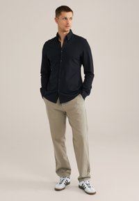 Črna srajca s srajčnim ovratnikom, dolgimi rokavi in oprijetim krojem. Kombinirana s svetlo kaki hlačami in belimi supergami s črnimi poudarki.