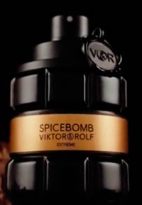 Flacon de parfum en forme de grenade noire avec une étiquette dorée portant l'inscription "SPICEBOMB VIKTOR & ROLF EXTREME" et un capuchon circulaire attaché par une chaîne.