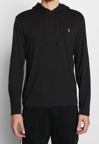 Svart långärmad hoodie i bomull med snörning, enkel design och en liten logotypaccents på bröstet.