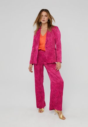 Pink leopard print suit with a fitted blazer and wide-leg trousers, paired with an orange v-neck top and gold high-heeled sandals.