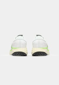 Running shoes in white mesh with lime green accents. Features a cushioned beige midsole and textured black rubber outsole. Rear view.