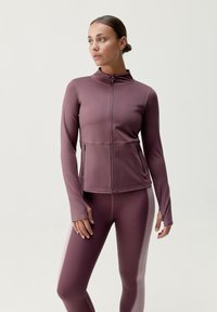 Langærmet atletisk jakke i dyb mauve, med fuld frontlynlås, to forlommer og tætsiddende design, parret med matchende tights.