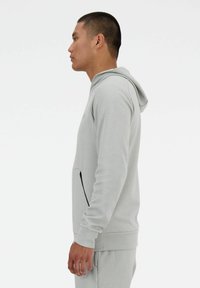 Felpa grigia chiara con cappuccio e tasca frontale dotata di una zip nera. Realizzata in materiale morbido, ha un design aderente e polsini a coste.