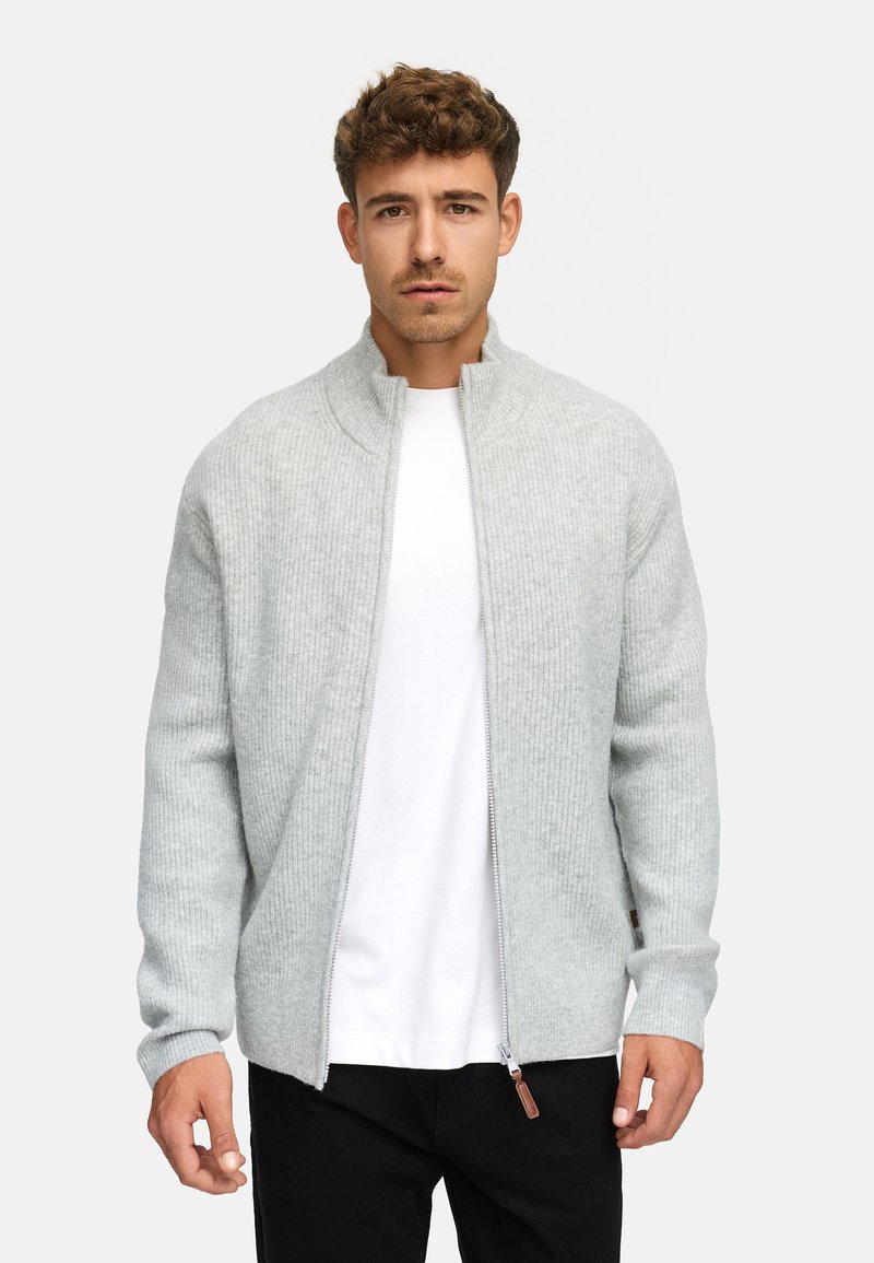 Cárdigan de canalé gris claro con cuello alto, cierre de cremallera y mangas largas, superpuesto a una camiseta blanca. Tejido de punto texturizado.