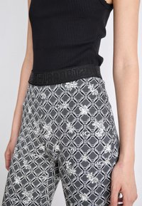 Schwarzes geripptes Tanktop kombiniert mit gemusterten Schwarz-Weiß-Leggings, die ein geometrisches Design und florale Akzente aufweisen. Schwarzer elastischer Bund.
