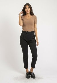 Haut marron côtelé à manches courtes associé à un pantalon noir taille haute avec une ceinture circulaire, complété par des mocassins noirs. Fond blanc.