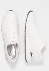 Sneaker bianchi in pelle con una texture liscia, dotati di un sistema di allacciatura, un accento metallico sul tallone e una suola in gomma con una presa testurizzata.