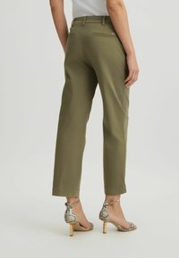 Pantaloni verde oliva con una vestibilità rilassata, dotati di due tasche posteriori e chiusura con zip. Abbinati a sandali con tacco a motivo serpente.