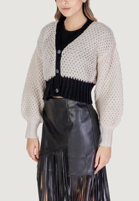 Cardigan lavorato all'uncinetto in crema e nero, con scollo a V, tre bottoni e maniche a palloncino, abbinato a una gonna in pelle nera con frange.