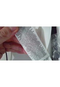Main tenant une étiquette en tissu blanche indiquant la composition du matériau et les instructions d'entretien en plusieurs langues.