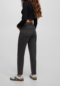 Svarta högmidjade jeans i tapered fit, med en sliten textur, bakfickor och tillsammans med vita sneakers med mörka detaljer.