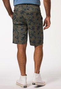 Pantaloni corti khaki con un motivo scuro di foglie di palma tropicali, vita elastica e tasche laterali, abbinati a sneakers alte bianche.
