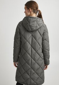 Gequilted lange jas in donkergrijs, met een capuchon en diagonaal stikselpatroon. Zachte textuur met een losvallende pasvorm, die tot halverwege de kuit reikt.