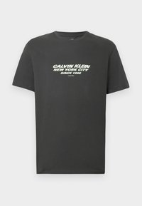 Ciemnoszary bawełniany t-shirt z krótkimi rękawami i okrągłym dekoltem. Z przodu biały i jasnopiaskowy napis: „CALVIN KLEIN NEW YORK CITY SINCE 1968.”
