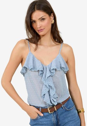 Himmelbluse, halbtransparent mit gerafften Spitzelementen und gepunkteter Struktur, kombiniert mit hochtaillierten Jeans und einem braunen Gürtel.