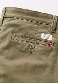 Olivgrüne Baumwollhose mit einer Gesäßtasche und einem grauen Knopf. Verfügt über ein gewebtes Etikett mit dem Text "Levi's" und roten Akzentnähten.