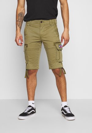 Cargo shorts in olive green cotton blend, featuring side pockets and adjustable drawstrings at the hem. Paired with black sneakers and white socks.