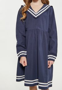 Laivastonsininen mekko, jossa on V-pääntie valkoisilla raidallisilla kauluksilla ja hihojen resoreilla, pitkät hihat, elastiset ranteet ja liehuva helma.