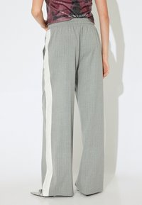 Lichtgrijze wijde broek met streepjes, voorzien van een witte zijstreep en een elastische tailleband. Soepele textuur met een ontspannen pasvorm.