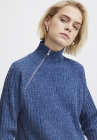 Sinine kudumiga särk kõrge kraega, millel on poolpikkus tõmblukk, soonikkoes tekstuur ja pikad varrukad. Pehme kangas ja mugav lõige.