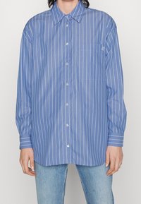 Blau gestreiftes Hemd mit Knopfleiste, Kragen, einer Brusttasche und langen Ärmeln. Leichter Stoff mit weißen vertikalen Streifen.