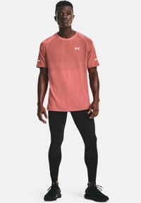 T-shirt atletico rosa con un motivo testurizzato, maniche corte e logo. Abbinato a leggings neri aderenti e scarpe sportive nere.