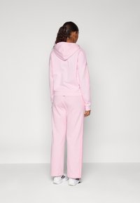 Vaatekappaleena on vaaleanpunainen fleece-huppari, jossa on huppu, väljä malli ja ribbaatut hihansuut, yhdistettynä yhteensopiviin verkkareihin, joissa on sivustrippi.