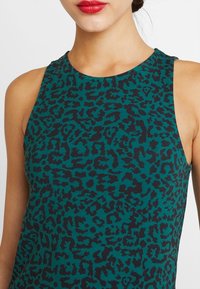 Bezrukávový top v teal barvě s černým leopardím vzorem. Disponuje vysokým výstřihem a jemnou texturou, ideální pro volnočasové nošení.