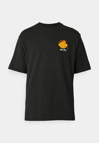 Camiseta de algodón negra de manga corta, con un gráfico colorido de "LEMON STAND" en el lado izquierdo del pecho. Diseño clásico de cuello crew.