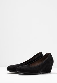 Sorte semsket kile sko med rund tå, lav hæl og glat overfladedesign; har en slip-on stil og blød indvendig foring.