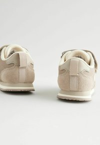 Beżowe buty sportowe z połączeniem gładkich i teksturowanych materiałów, z rzepem, wyściełanym kołnierzem i jasnymi gumowymi podeszwami.