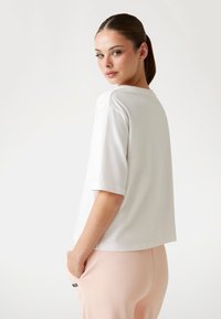 T-shirt bianco a maniche corte con vestibilità rilassata e collo rotondo, mostrato dal retro, realizzato in morbido tessuto di cotone.