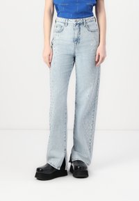 Jeans de mezclilla de pierna ancha en un tono azul claro, con tachuelas plateadas a lo largo de los lados, que cuentan con un detalle de cremallera en el dobladillo y un diseño clásico de cinco bolsillos.