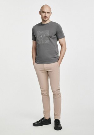 Szary t-shirt z krótkim rękawem z kwadratowym wzorem graficznym; beżowe slim fit spodnie; czarne buty; minimalistyczny wygląd.
