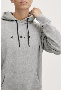 Felpa grigia con cappuccio e coulisse, con la scritta nera "A.R.C." sul petto. Tessuto morbido, tasca frontale e polsini a coste.