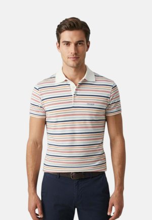 Giovane uomo che indossa una polo a maniche corte con righe orizzontali rosse, blu e beige e pantaloni blu scuro con cintura nera.