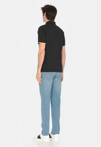 Polo nero con dettagli gialli col colletto e sulle maniche, abbinato a pantaloni di jeans blu chiaro e sneaker bianche.