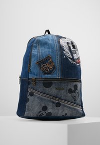 Džínový batoh s přední kapsou a různými texturami, s výrazným motivem Mickey Mouse a dekorativním prošitím v modrých odstínech.